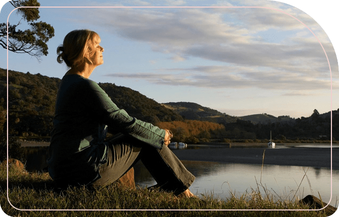 A woman sitting on the grass near water.