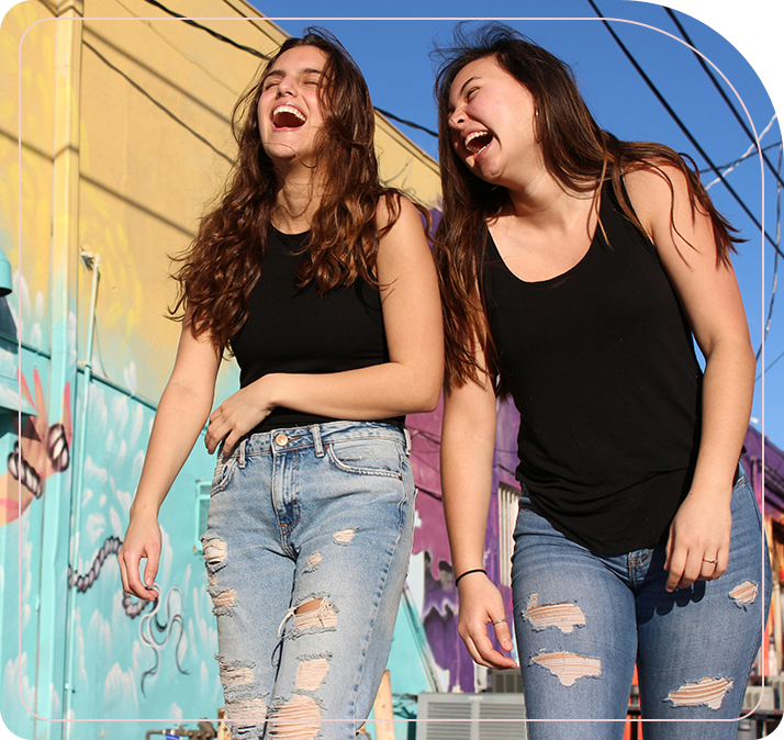 Two women laugh while standing next to each other.